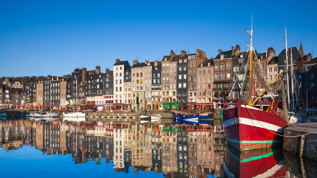 Port de Honfleur avec bateaux et façades colorées reflétées dans l’eau, découverte artistique et historique de la ville normande en 2026.