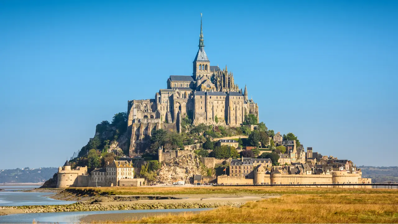 Vue panoramique du Mont-Saint-Michel et de son abbaye entourée des remparts, destination phare pour des vacances en Normandie avec itinéraires et visites en 2026.